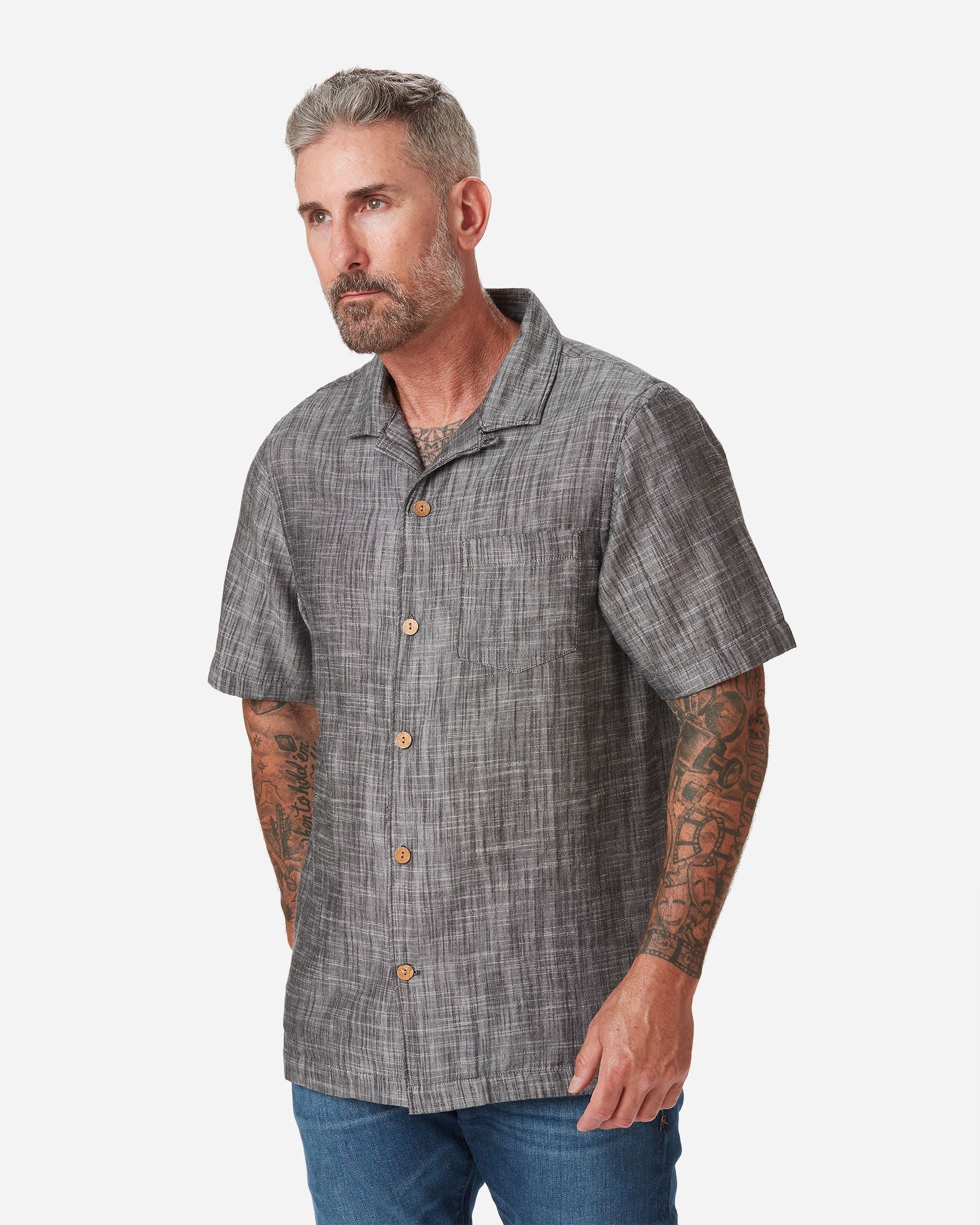 Model with a front and rightward gaze wearing Ace Rivington "Black" Double gauze soft-textured cotton fabric camp collar shirt with coconut buttons and left-breast pocket and a pair of Ace Rivington dark vintage blue denim jeans