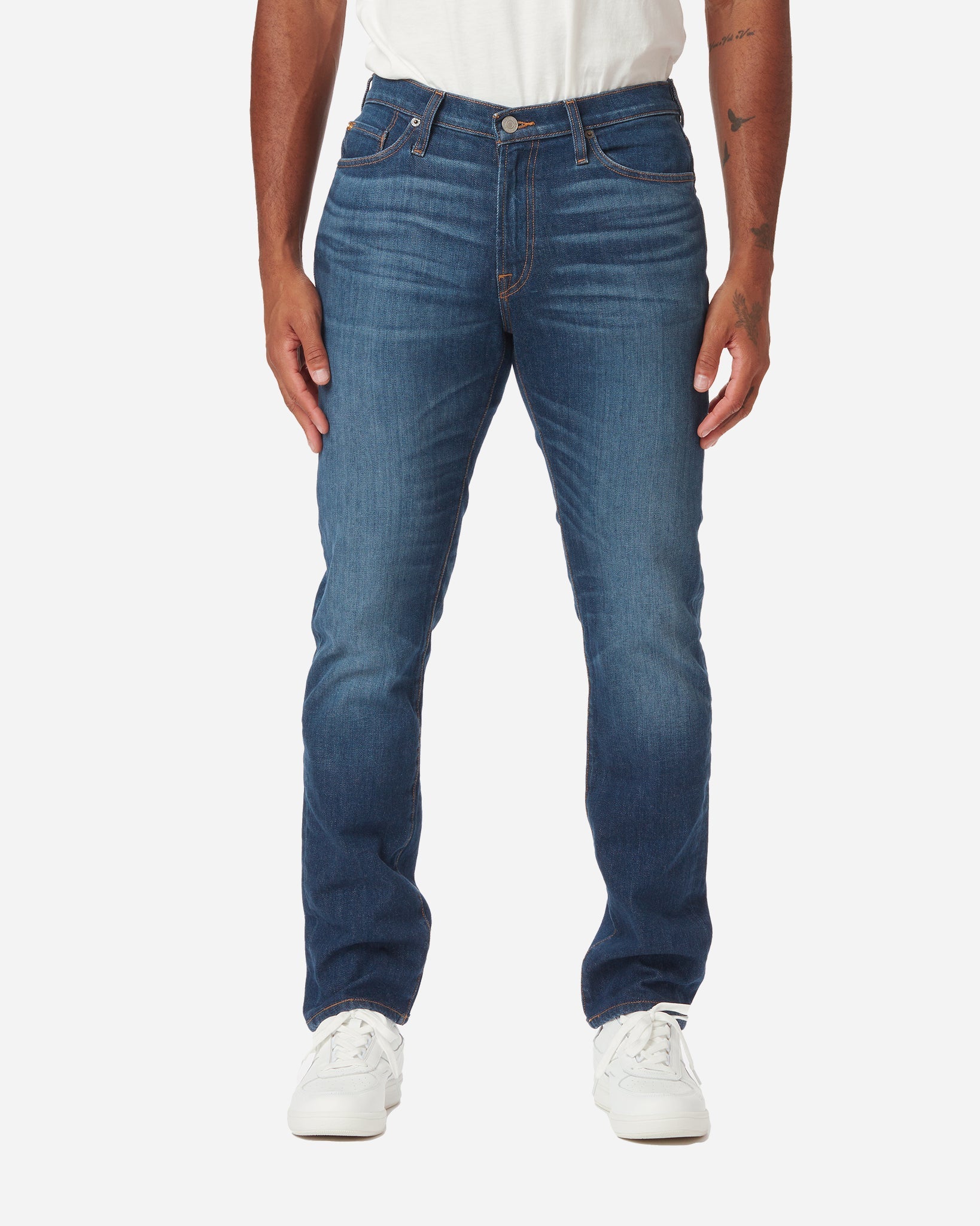 Model facing directly forward wearing a pair of Ace Rivington dark blue athletic taper denim jeans with light stylistic fabric wear on the thigh area with a pair of white Diadora B Elite sneaker shoes and tucked white Ace Rivington super soft supima short-sleeved tee shirt